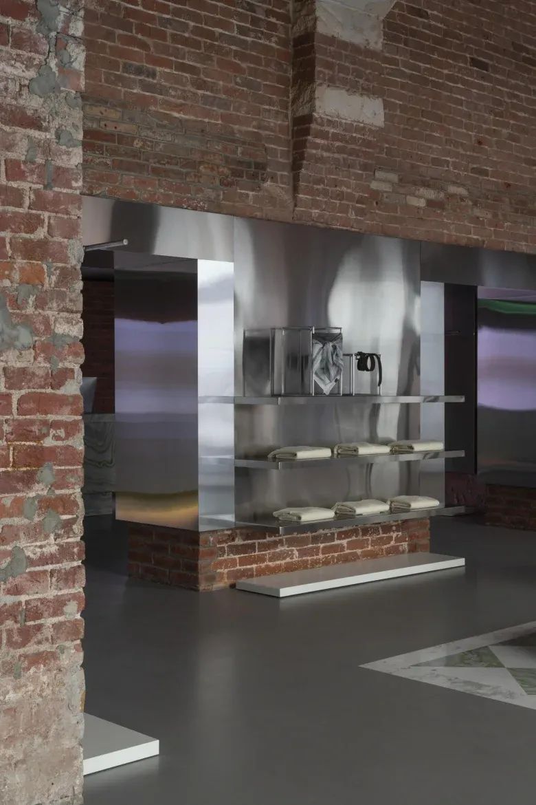 Металлические полки с одеждой на кирпичной стене NUDE STORY store