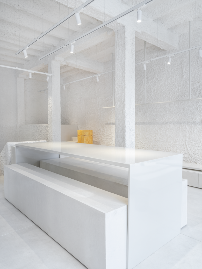 Центральный стол и лавки в белом интерьере магазина Thinking MU Store